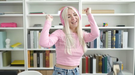 Téléchargez les photos : Young blonde woman student listening to music and dancing at library university - en image libre de droit