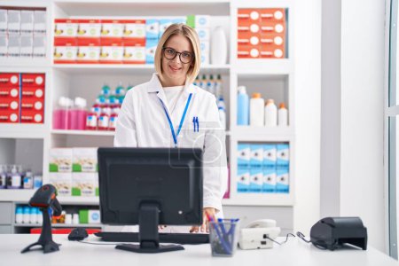 Photo for Young blonde woman pharmacist smiling confident using computer at pharmacy - Royalty Free Image