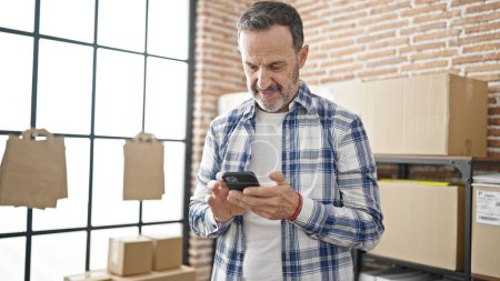 Téléchargez les photos : Homme d'âge moyen e-commerce travailleur d'affaires en utilisant smartphone au bureau - en image libre de droit