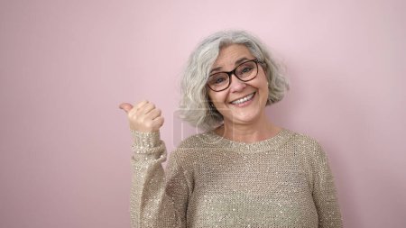 Téléchargez les photos : Middle age woman with grey hair smiling confident pointing to the side over isolated pink background - en image libre de droit