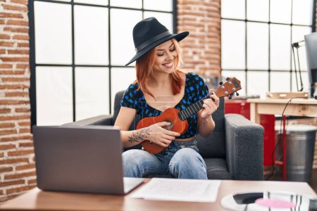 Foto de Joven mujer caucásica músico sonriendo confiado jugando ukelele en estudio de música - Imagen libre de derechos