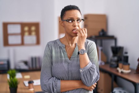 Foto de Mujer afroamericana que trabaja en la oficina con gafas que se ven estresadas y nerviosas con las manos en la boca mordiendo uñas. problema de ansiedad. - Imagen libre de derechos