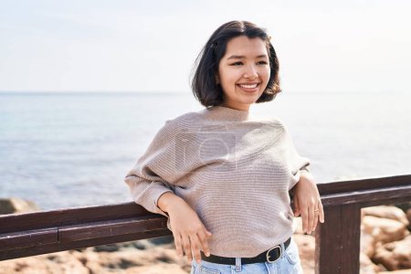 Téléchargez les photos : Young woman smiling confident looking to the side at seaside - en image libre de droit