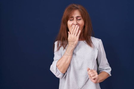 Photo for Middle age woman standing over blue background bored yawning tired covering mouth with hand. restless and sleepiness. - Royalty Free Image