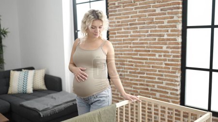 Téléchargez les photos : Jeune femme enceinte touchant le ventre debout au berceau à la maison - en image libre de droit
