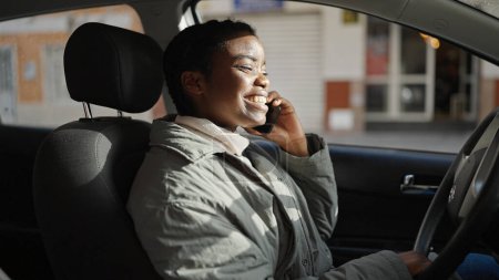 Photo for African american woman talking on smartphone sitting on car at street - Royalty Free Image