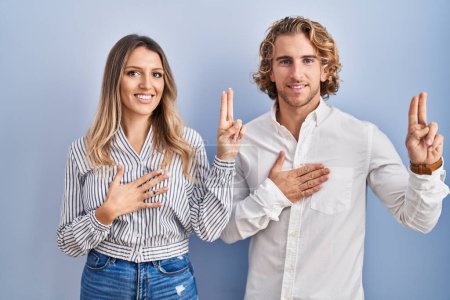 Photo for Young couple standing over blue background smiling swearing with hand on chest and fingers up, making a loyalty promise oath - Royalty Free Image