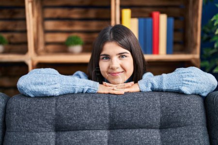 Téléchargez les photos : Jeune belle femme hispanique souriant confiant appuyé sur le canapé à la maison - en image libre de droit