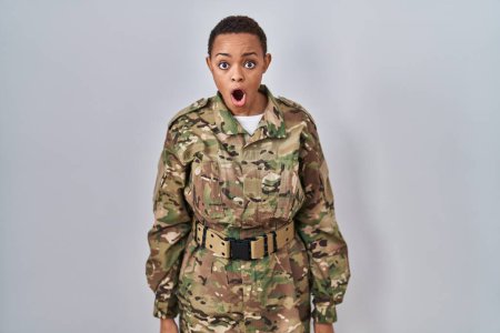 Foto de Hermosa mujer afroamericana vistiendo camuflaje ejército uniforme miedo y conmocionado con sorpresa y expresión asombrada, miedo y cara emocionada. - Imagen libre de derechos