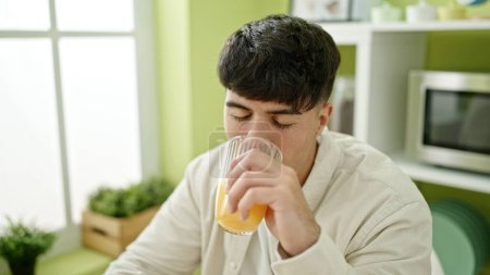 Photo for Young hispanic man drinking orange juice sitting on table at dinning room - Royalty Free Image