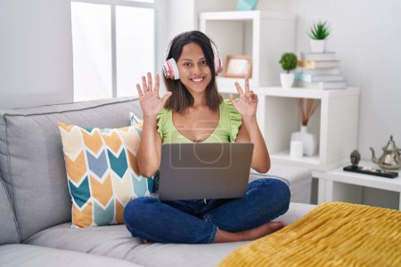 Photo for Hispanic young woman using laptop at home showing and pointing up with fingers number eight while smiling confident and happy. - Royalty Free Image