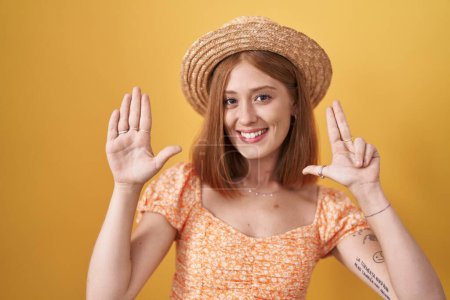 Photo for Young redhead woman standing over yellow background wearing summer hat showing and pointing up with fingers number eight while smiling confident and happy. - Royalty Free Image