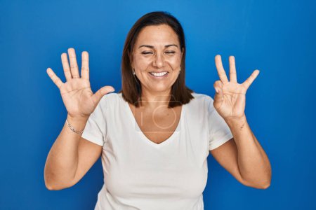 Photo for Hispanic mature woman standing over blue background showing and pointing up with fingers number eight while smiling confident and happy. - Royalty Free Image
