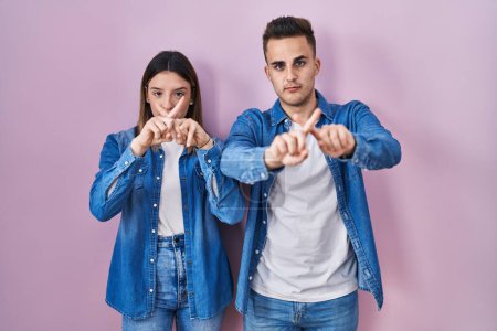 Téléchargez les photos : Jeune couple hispanique debout sur fond rose expression de rejet croisant les doigts faisant signe négatif - en image libre de droit