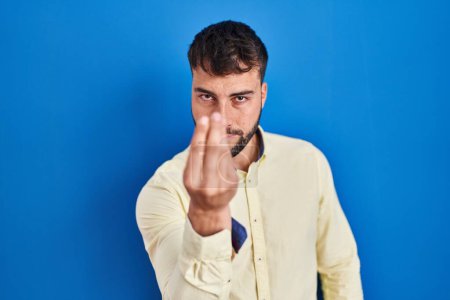 Foto de Hombre hispano guapo de pie sobre fondo azul haciendo gesto italiano con la mano y los dedos expresión de confianza - Imagen libre de derechos
