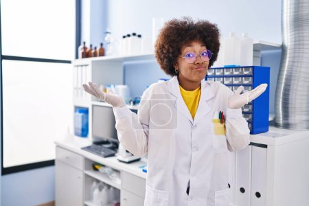Foto de Mujer afroamericana joven que trabaja en el laboratorio científico gritando y gritando fuerte a un lado con la mano en la boca. concepto de comunicación. - Imagen libre de derechos