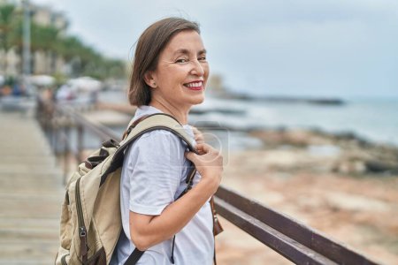 Foto de Mujer de mediana edad turista sonriendo confiado usando mochila en la playa - Imagen libre de derechos