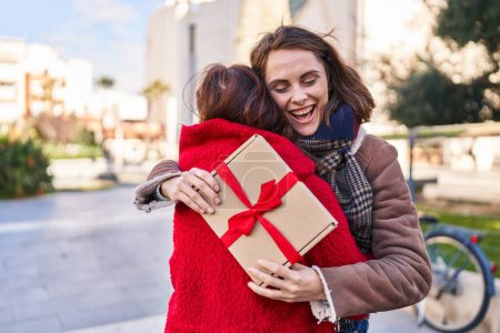 Téléchargez les photos : Deux femmes mère et fille étreignant l'autre surprise avec un cadeau au parc - en image libre de droit