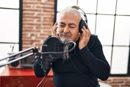 Foto de Hombre músico de pelo gris de mediana edad sonriendo confiado cantando canción en el estudio de música - Imagen libre de derechos