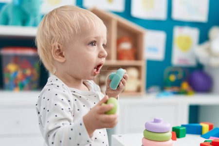 Téléchargez les photos : Adorable bambin blond jouant avec des jouets debout à la maternelle - en image libre de droit