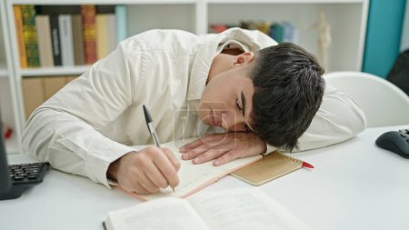 Photo for Young hispanic man student writing notes tired at library university - Royalty Free Image