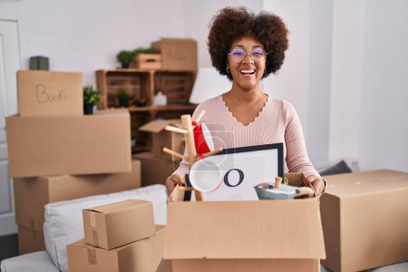 Téléchargez les photos : Jeune femme afro-américaine déménageant dans une nouvelle maison souriant et riant fort à haute voix parce que drôle blague folle. - en image libre de droit