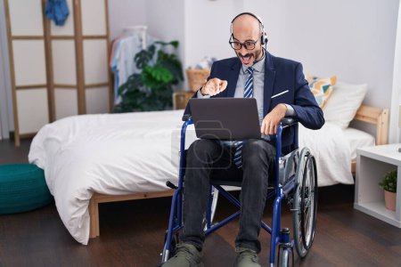 Téléchargez les photos : Homme hispanique avec barbe assis sur fauteuil roulant faisant affaires appel vidéo souriant heureux pointant avec la main et le doigt - en image libre de droit