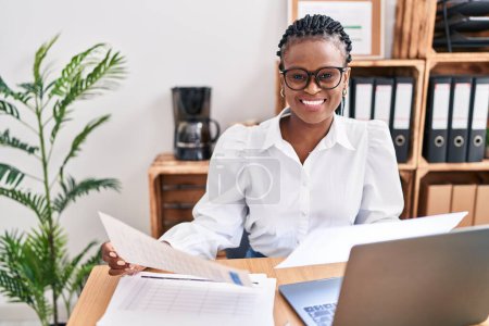 Téléchargez les photos : Femme afro-américaine travailleur d'affaires en utilisant un ordinateur portable document de lecture au bureau - en image libre de droit