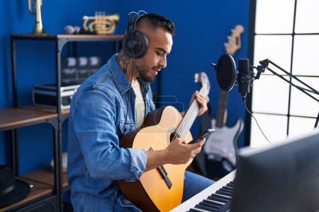 Téléchargez les photos : Jeune artiste hispanique utilisant un smartphone jouant de la guitare classique au studio de musique - en image libre de droit