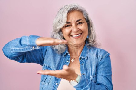 Photo for Middle age woman with grey hair standing over pink background gesturing with hands showing big and large size sign, measure symbol. smiling looking at the camera. measuring concept. - Royalty Free Image