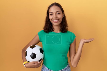 Téléchargez les photos : Jeune femme hispanique tenant ballon souriant joyeuse présentation et pointant avec la paume de la main en regardant la caméra. - en image libre de droit