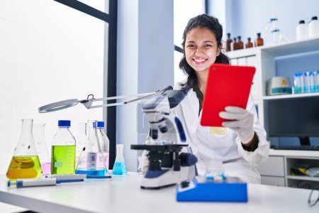 Téléchargez les photos : Jeune scientifique latino-américaine utilisant le microscope et le pavé tactile au laboratoire - en image libre de droit