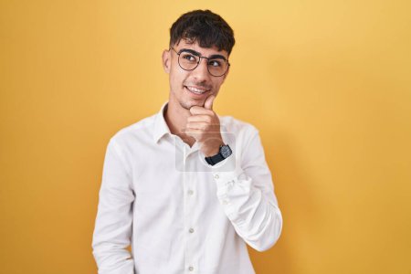 Photo for Young hispanic man standing over yellow background with hand on chin thinking about question, pensive expression. smiling and thoughtful face. doubt concept. - Royalty Free Image