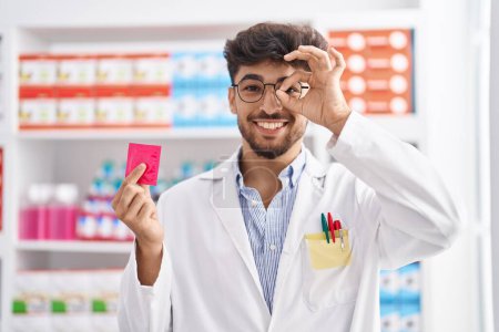 Foto de Hombre árabe con barba trabajando en farmacia sosteniendo condón celebrando loco y sorprendido por el éxito con los ojos abiertos gritando emocionado. - Imagen libre de derechos