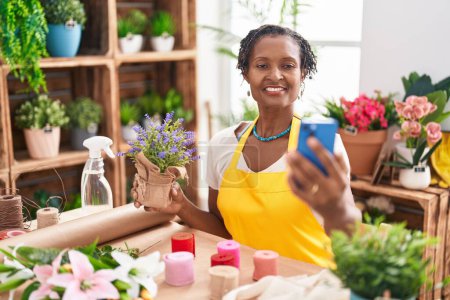 Photo for Middle age african american woman florist make selfie by smartphone holding lavender plant at flower shop - Royalty Free Image