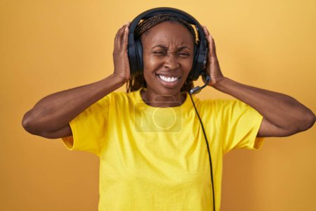 Photo for African american woman listening to music using headphones covering ears with fingers with annoyed expression for the noise of loud music. deaf concept. - Royalty Free Image