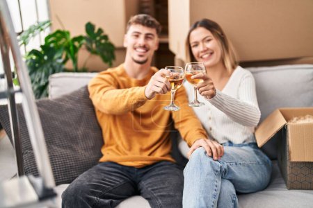 Photo for Young man and woman couple toasting with wine sitting on sofa at new home - Royalty Free Image