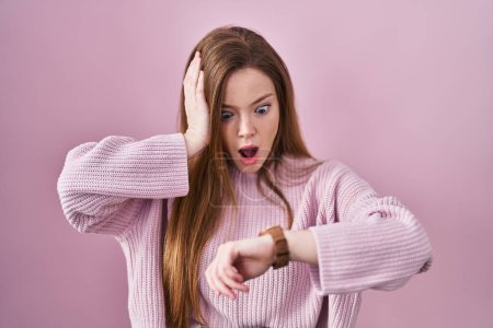 Photo for Young caucasian woman standing over pink background looking at the watch time worried, afraid of getting late - Royalty Free Image