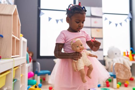 Téléchargez les photos : Africaine américaine fille tenant bébé poupée debout à la maternelle - en image libre de droit