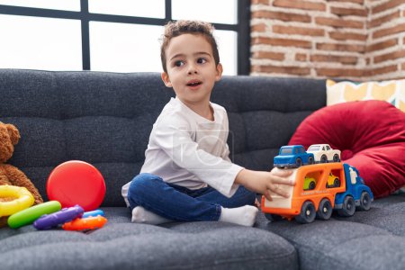 Foto de Adorable chico hispano jugando con juguete de coche sentado en el sofá en casa - Imagen libre de derechos