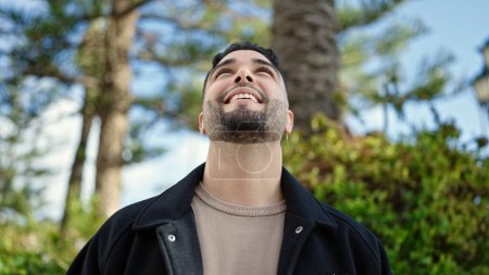 Foto de Hombre árabe joven sonriendo confiado mirando al cielo en el parque - Imagen libre de derechos