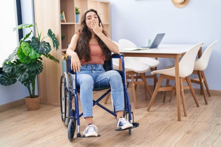 Photo for Young teenager girl sitting on wheelchair at the living room covering mouth with hand, shocked and afraid for mistake. surprised expression - Royalty Free Image