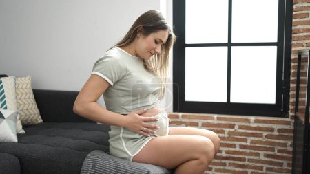 Téléchargez les photos : Jeune femme enceinte souriant confiant toucher le ventre à la maison - en image libre de droit