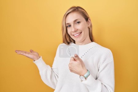 Téléchargez les photos : Jeune femme caucasienne portant un pull blanc sur fond jaune montrant la main de la paume et faisant un geste correct avec les pouces levés, souriant heureux et joyeux - en image libre de droit