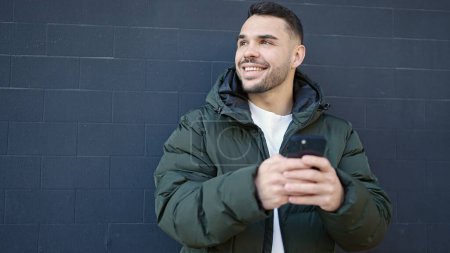 Téléchargez les photos : Jeune homme hispanique souriant confiant en utilisant smartphone sur fond noir isolé - en image libre de droit
