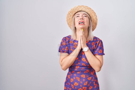 Photo for Young caucasian woman wearing flowers dress and summer hat begging and praying with hands together with hope expression on face very emotional and worried. begging. - Royalty Free Image