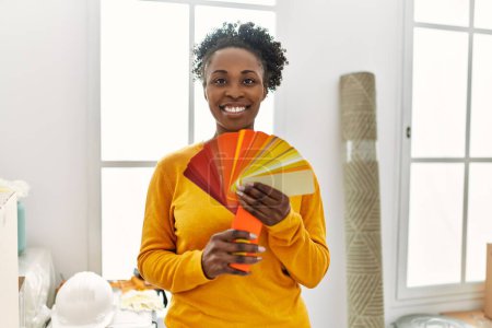 Foto de Mujer afroamericana sonriendo confiada sosteniendo prueba de color en nuevo hogar - Imagen libre de derechos