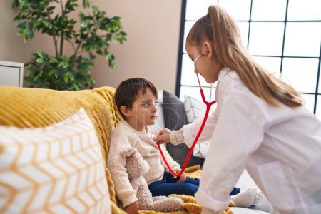 Photo for Adorable boy and girl wearing doctor uniform examining with stethoscope at home - Royalty Free Image