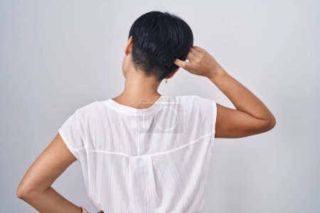 Foto de Joven mujer asiática con pelo corto de pie sobre fondo aislado hacia atrás pensando en la duda con la mano en la cabeza - Imagen libre de derechos