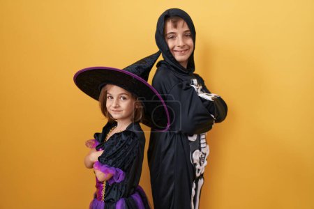 Photo for Adorable boy and girl wearing halloween costume standing with arms crossed gesture over isolated yellow background - Royalty Free Image